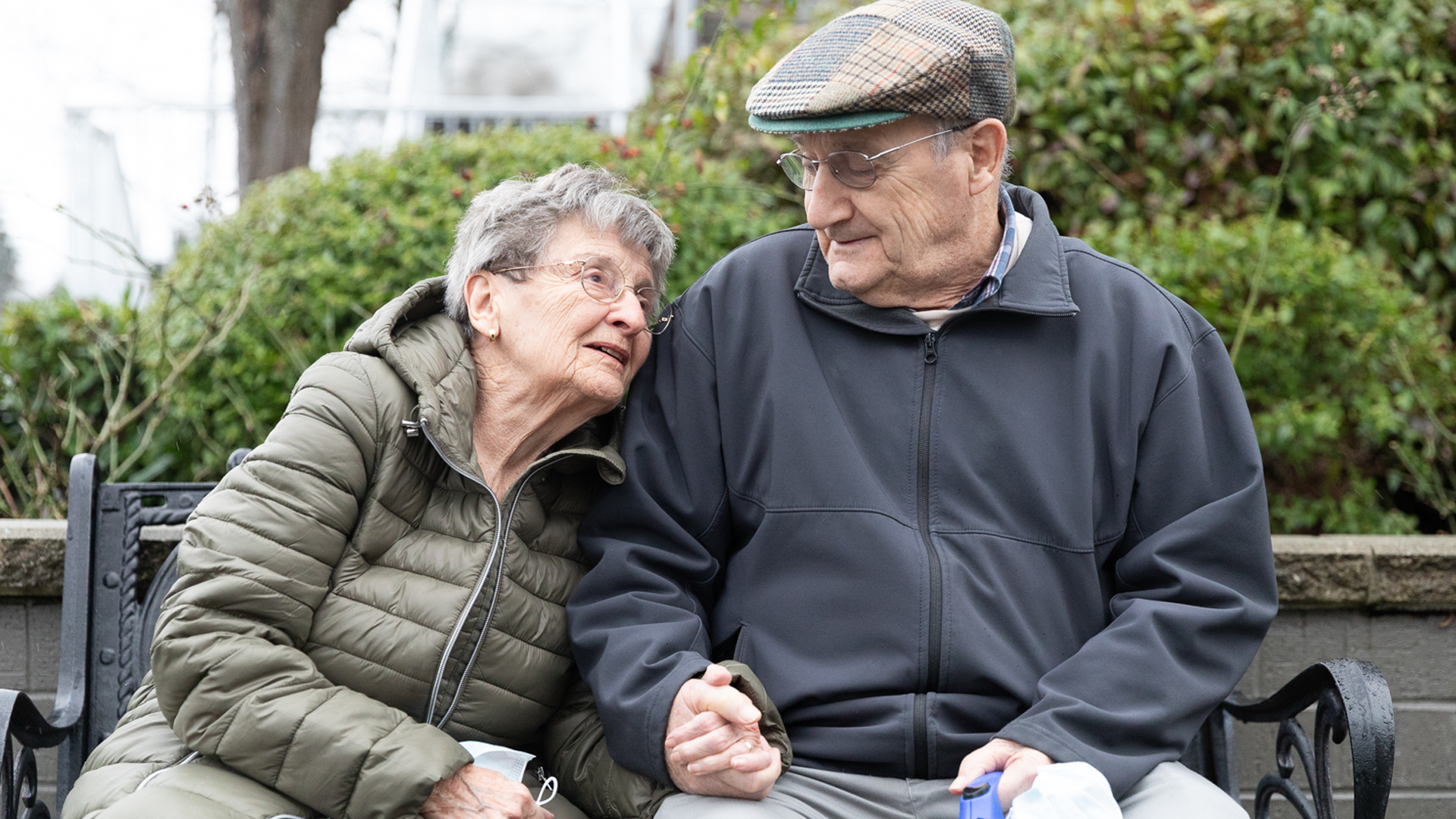 An senior couple holding hands sitting on a park bench