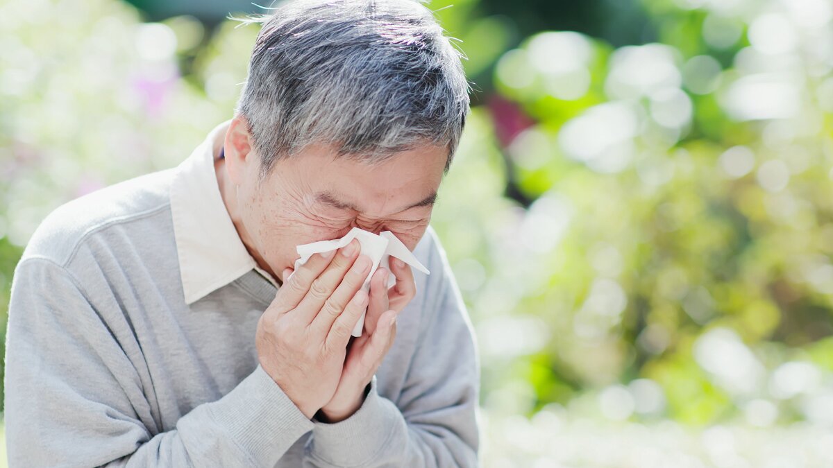 A picture of elderly man sneezing outside his senior care home