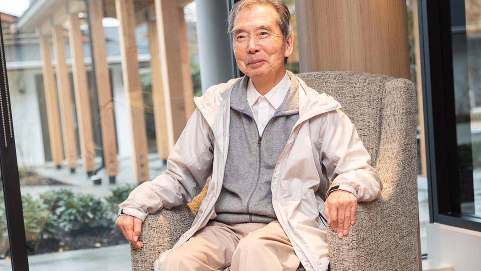 An elderly man smiling while sitting in a chair in senior housing