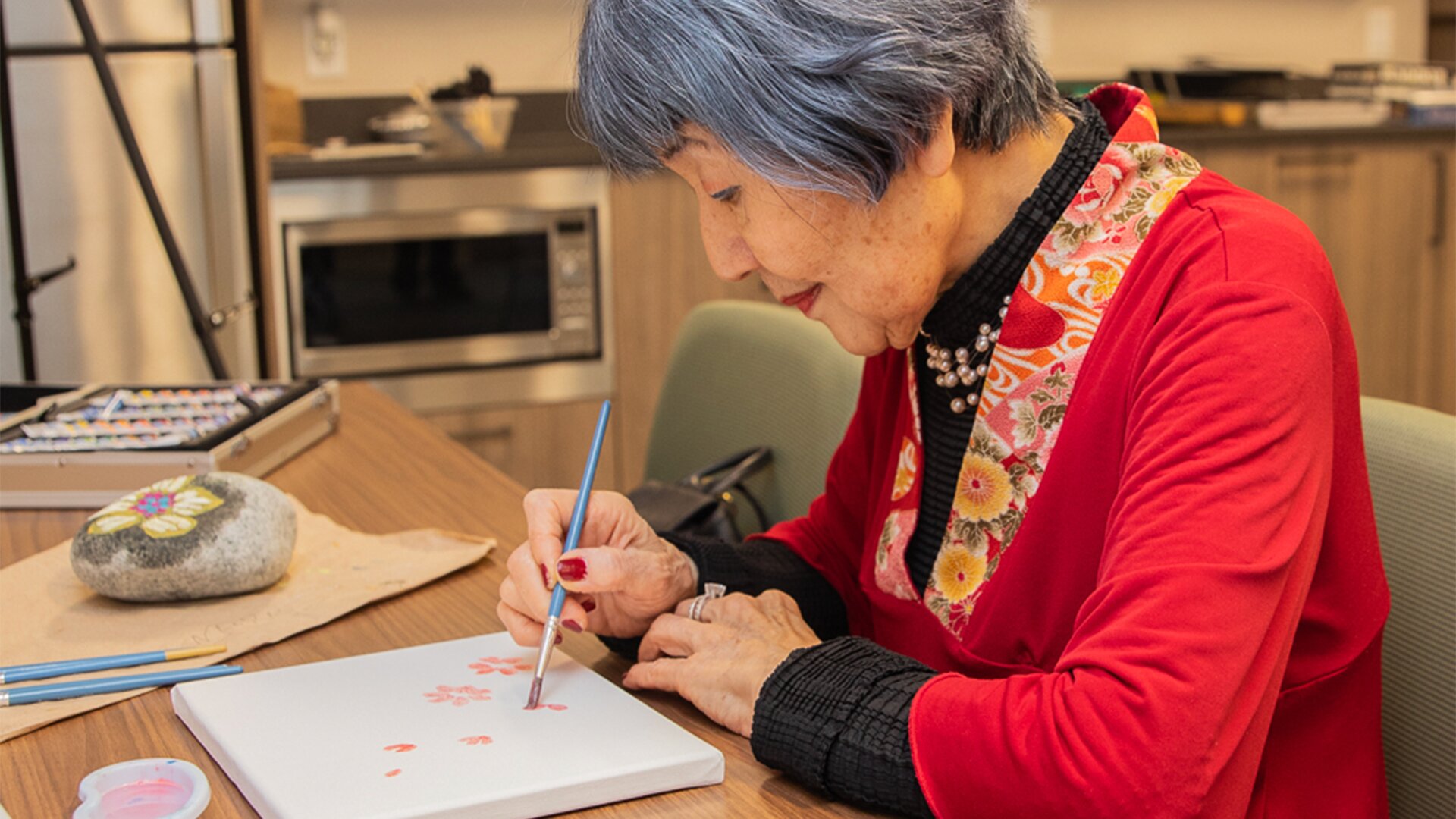 An elderly woman painting a canvas of flowers, activities for seniors at Wisteria Place