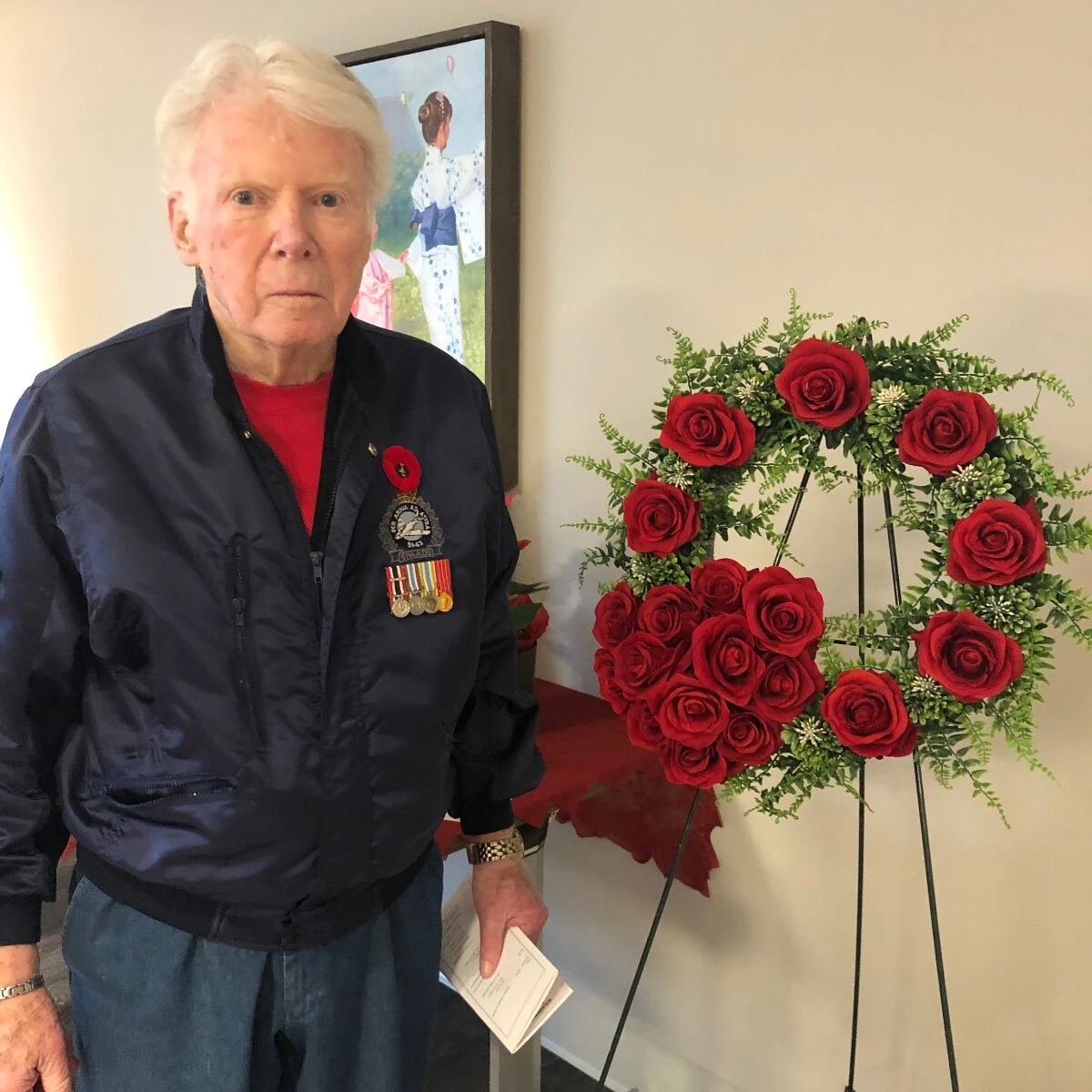 An elderly man stand with a red roses on Remembrance Day in his senior home