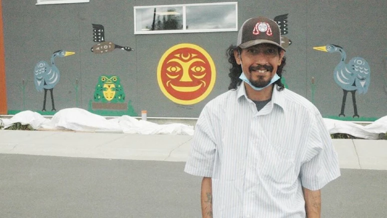 An indigenous man standing in front of artwork on a wall