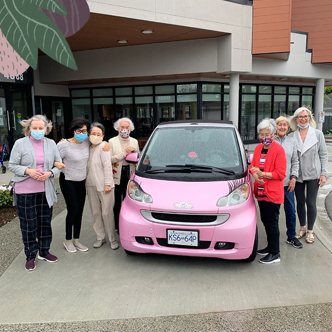 A group of elderly ladies with a pink car outside a seniors home