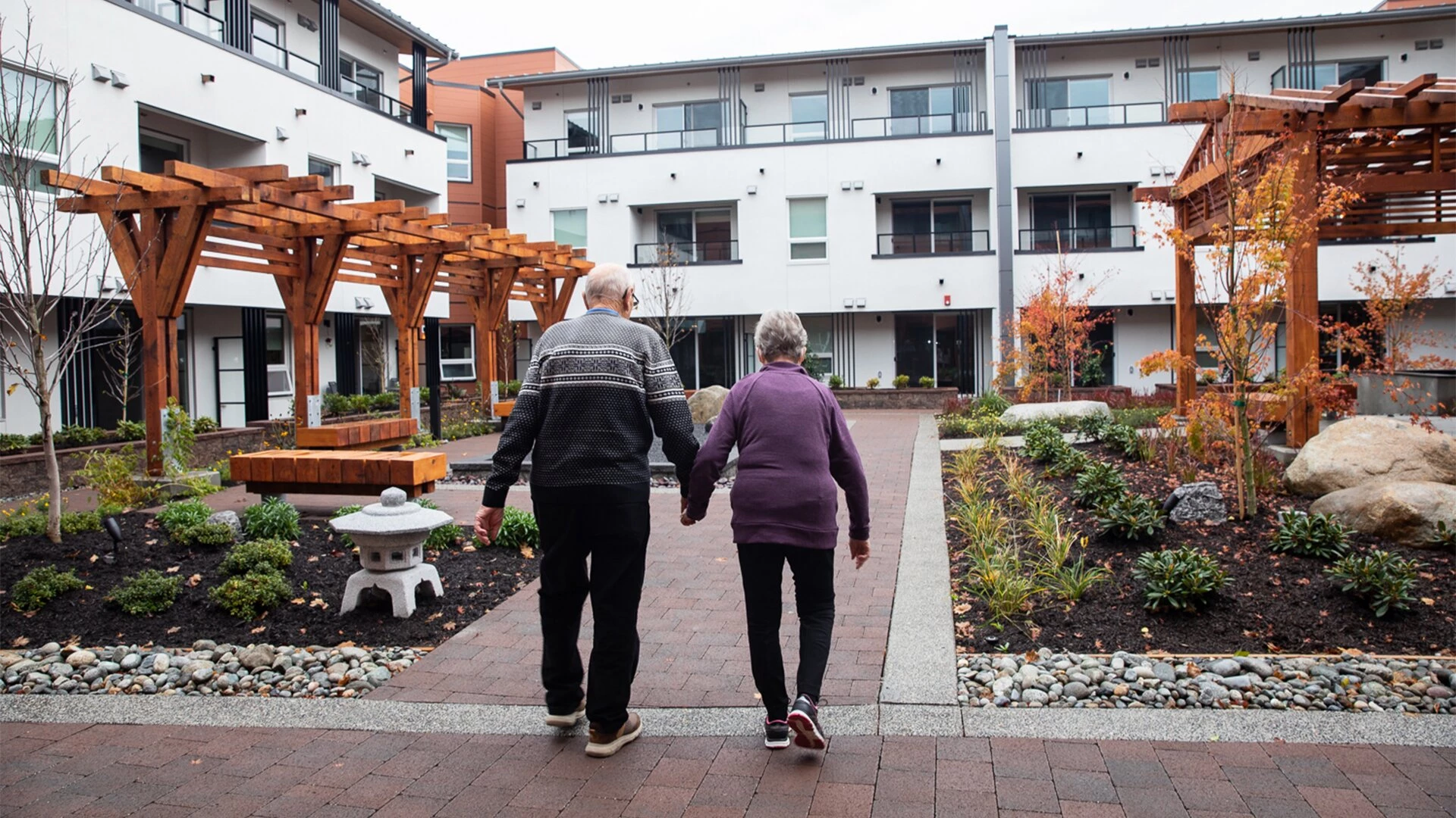 An elderly couple holding hands and walking in a courtyard in independent living for seniors