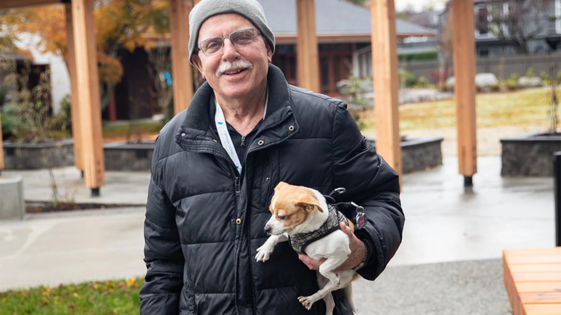 A senior man holding a dog in his arms outside senior housing
