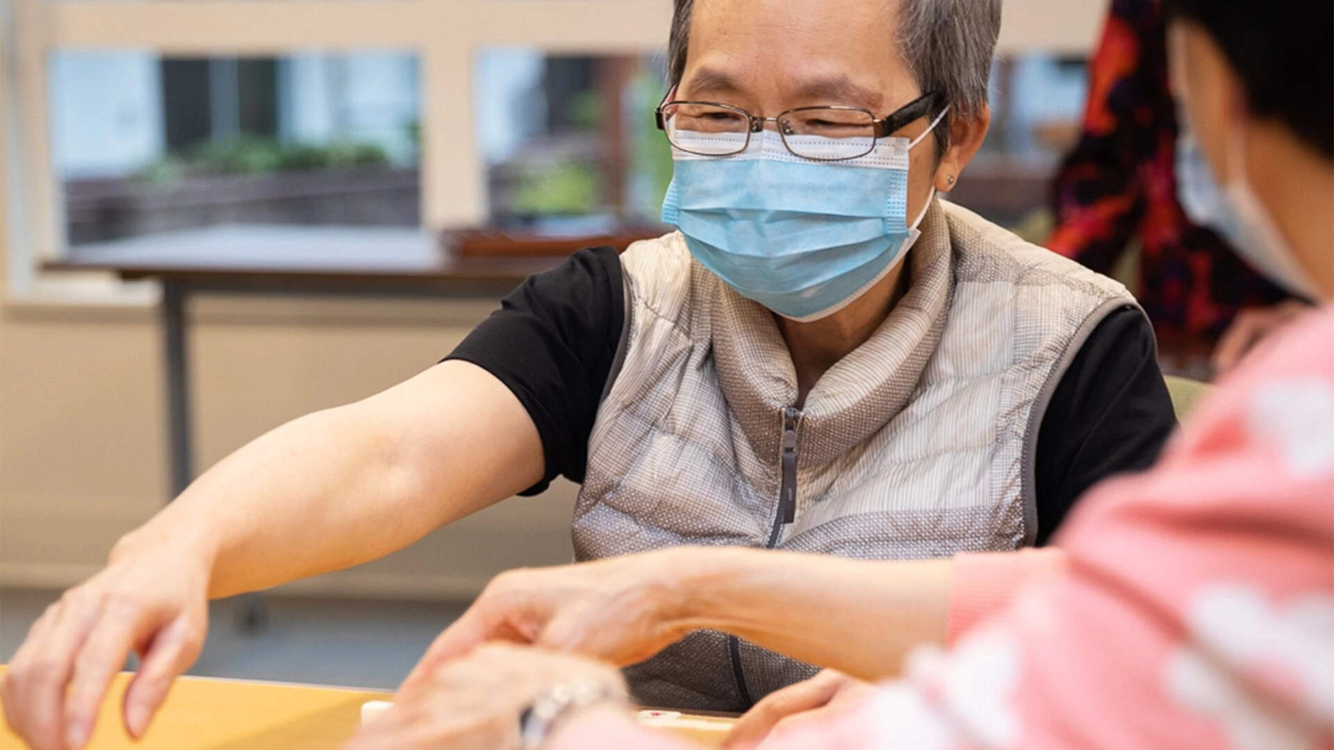 An elderly woman wearing a mask and playing mahjong in senior living