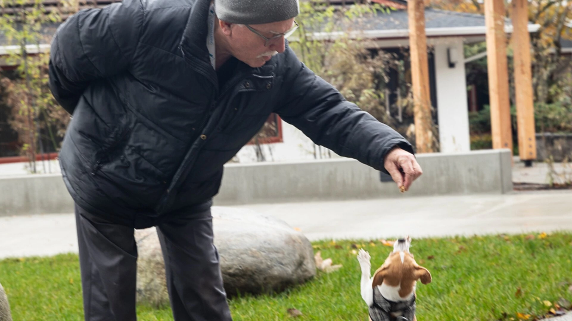 A man wearing a winter coat playing with his dog in a courtyard outside his retirement home