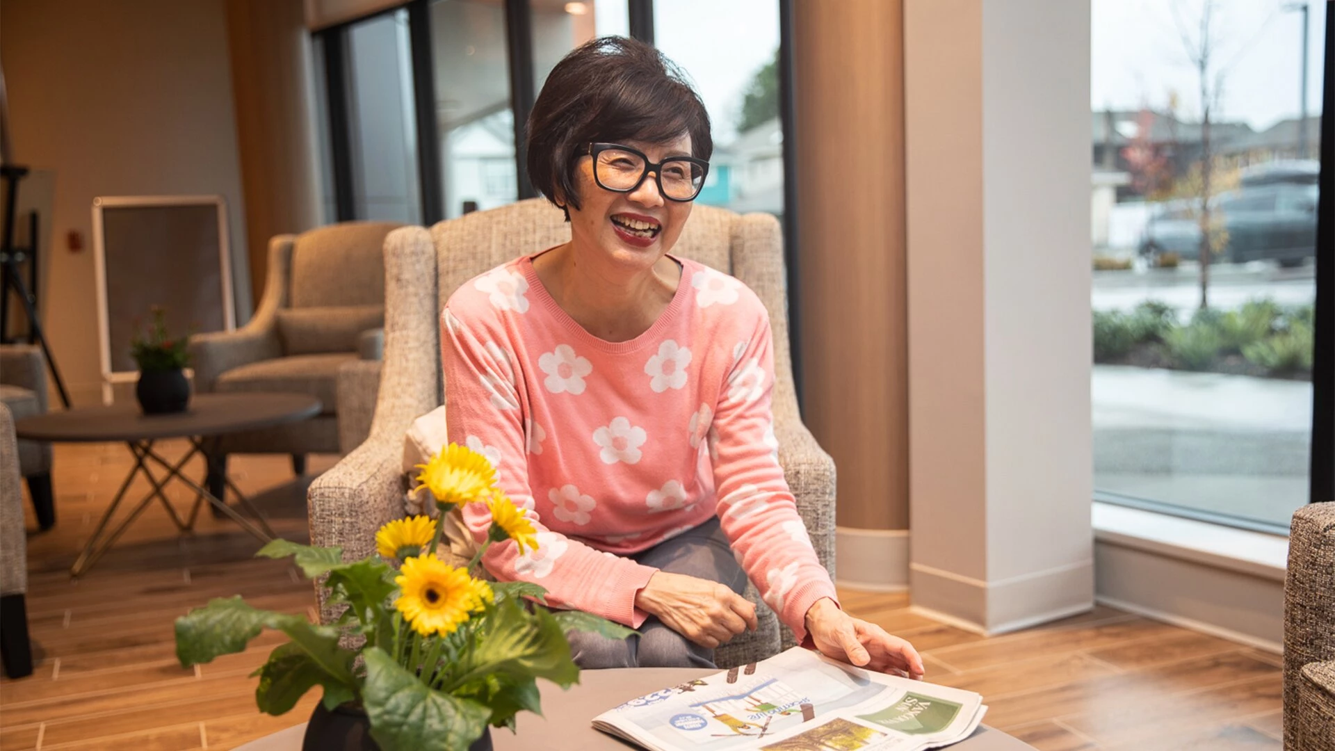 An senior lady smiling while reading the newspaper in senior apartments