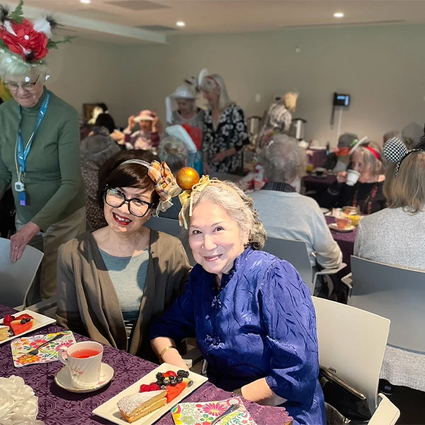 Two senior women seated together smiling with tea and dessert in front of them