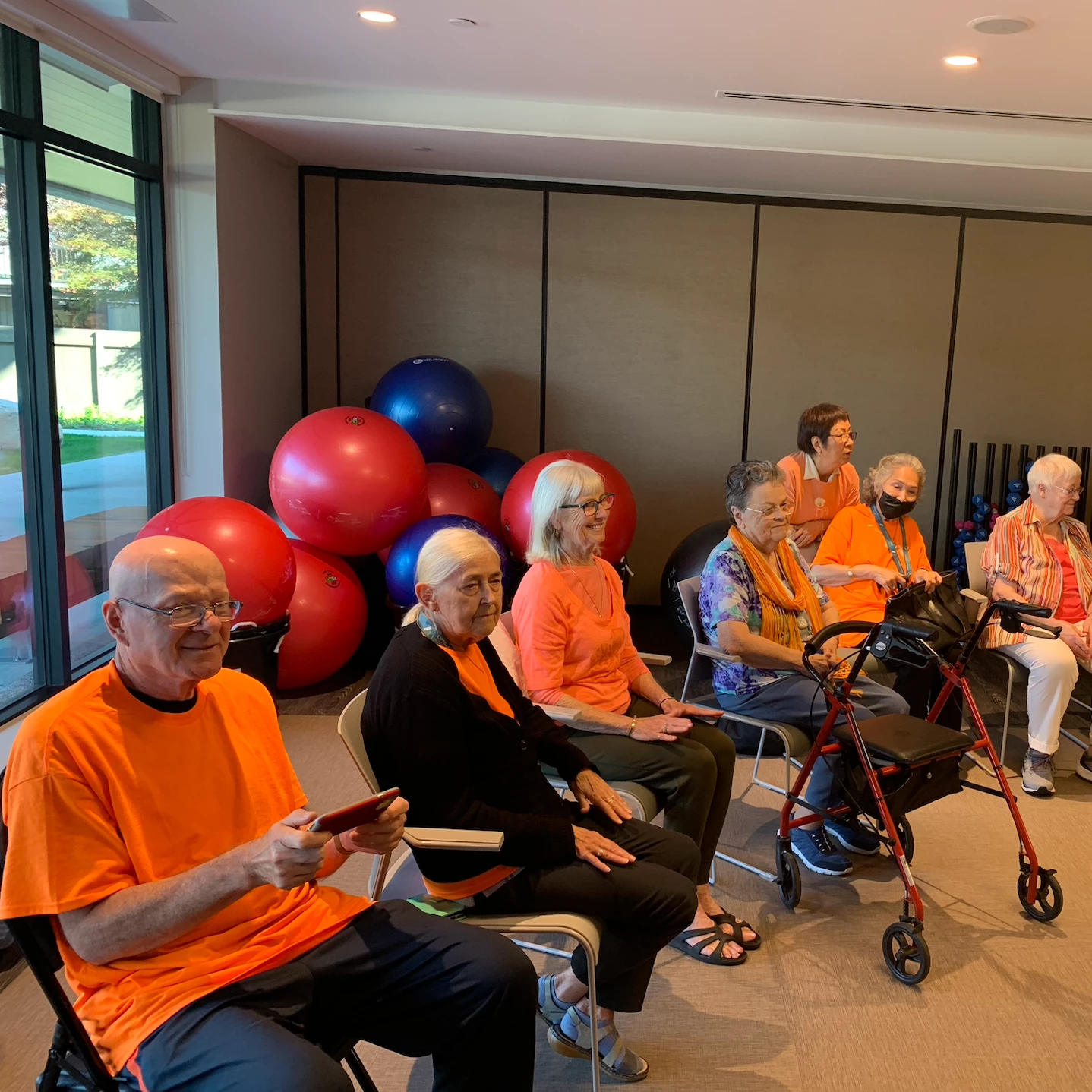 Residents of a senior home in orange attire all seated together.