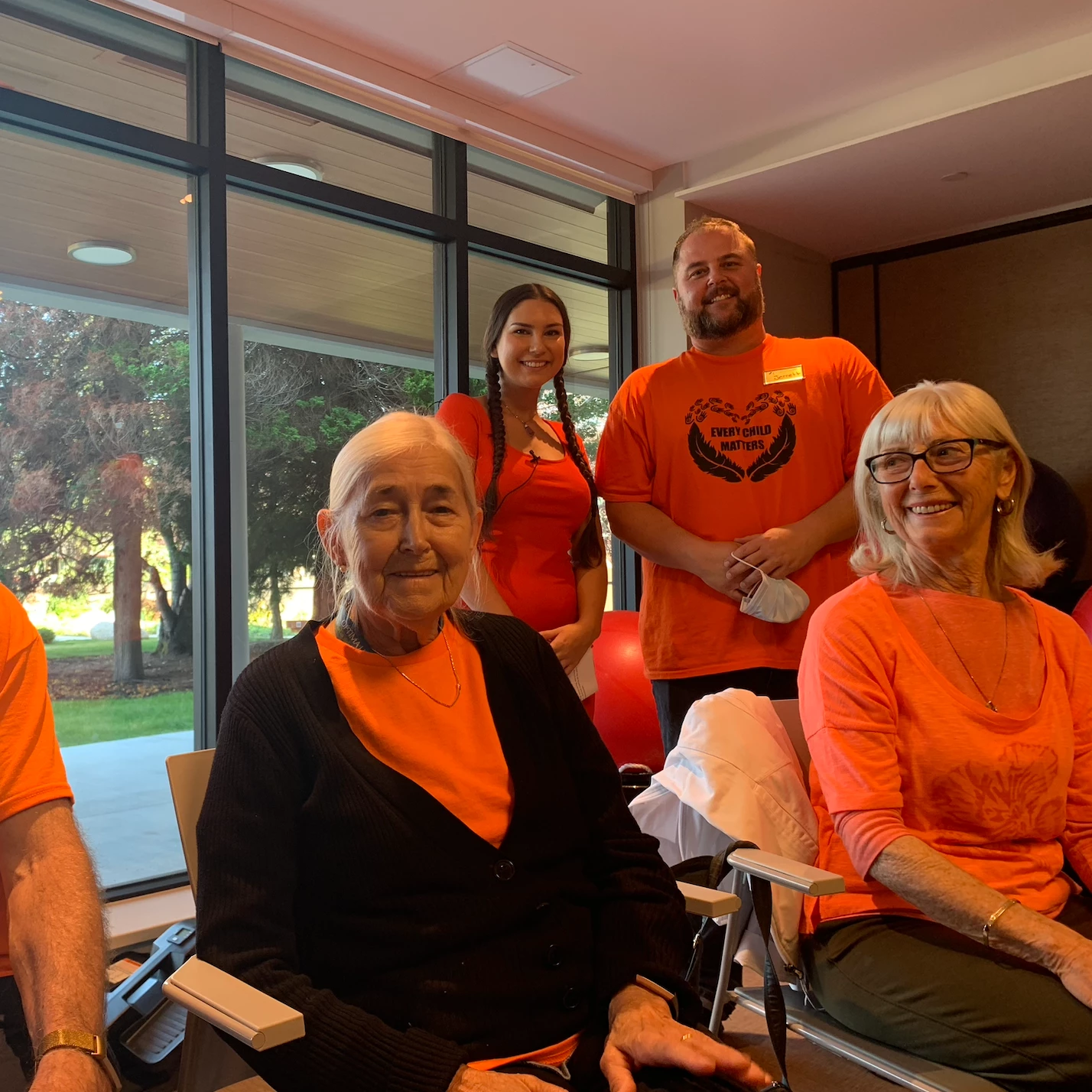 Residents of a senior home smiling with staff wearing orange for Truth and Reconciliation day. One shirt says, 